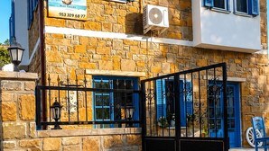 Un edificio de piedra de dos pisos con contraventanas azules, un letrero y una reja negra.