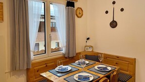 Et spiseområde med et træbord dækket til fire personer, et ur på væggen og et vindue med gardiner.