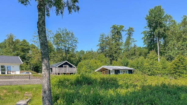 En stuga med en veranda, omgiven av tät skog och en klar himmel.