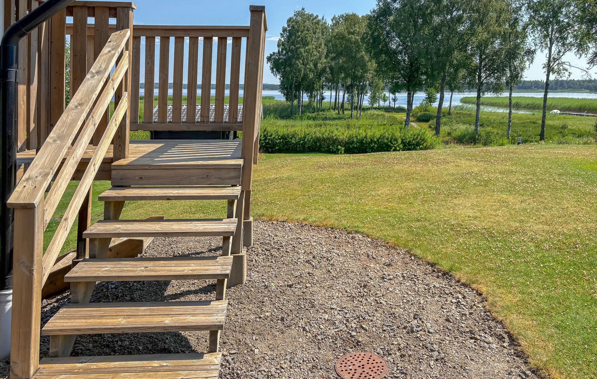 Une terrasse en bois avec des marches menant à un espace abrité, entourée d’un champ herbeux et d’arbres.