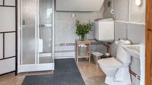 Ett badrum med en duschkabin i glas, en toalett, ett handfat och en liten träpall med en korg.