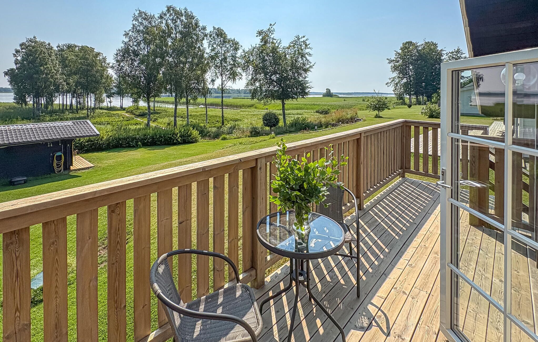 Une terrasse en bois avec une table et des chaises en verre, donnant sur une pelouse et des arbres.