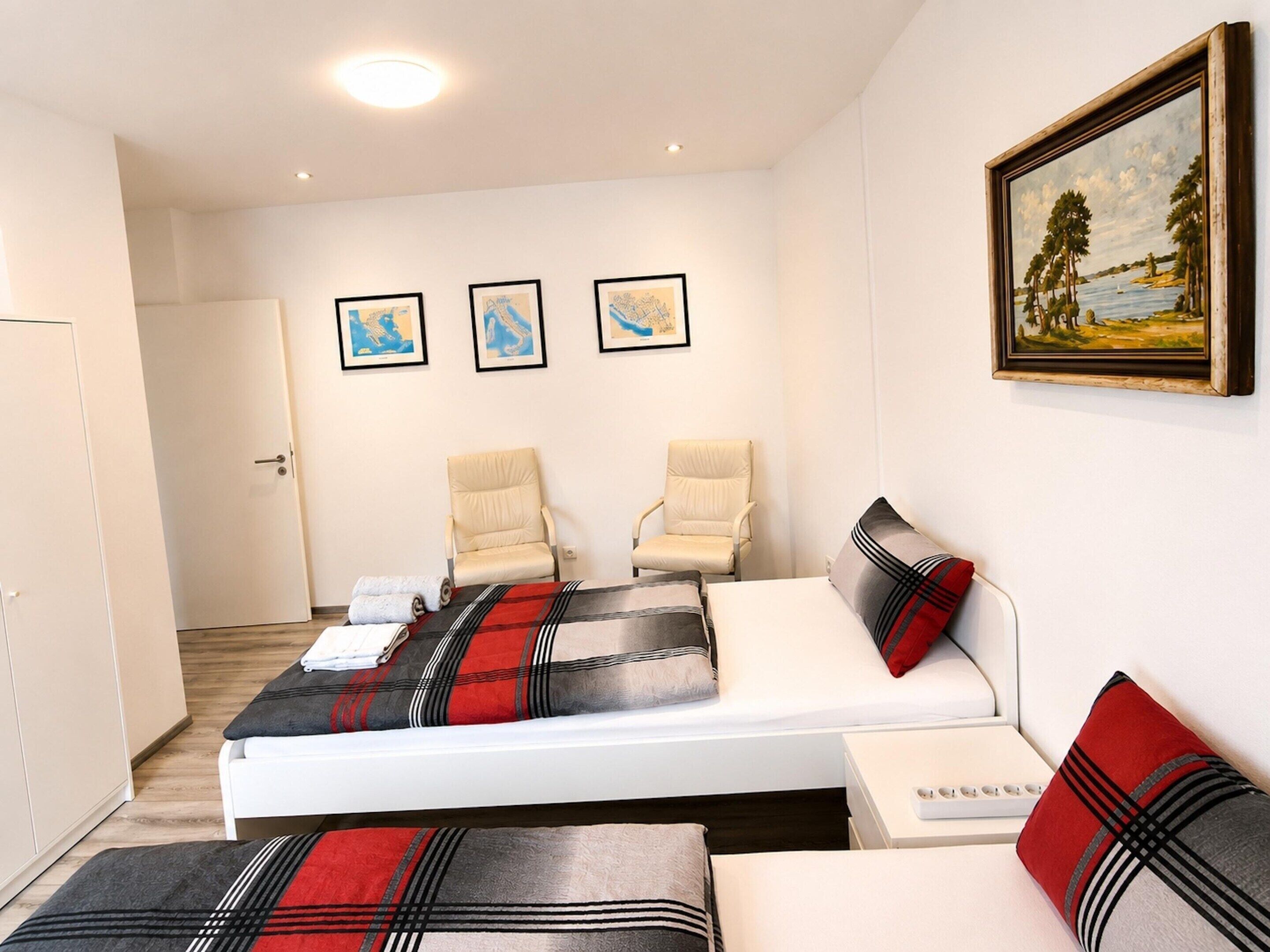A bedroom with a bed, two chairs, a painting, and a bedside table.