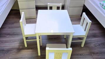 A small, clean room with a white table and four chairs, a bedside table, and a nightstand.