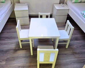 Una habitación pequeña y limpia con una mesa blanca y cuatro sillas, una mesita de noche y un tocador.