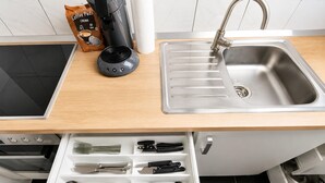 A kitchen with a coffee maker, a coffee pod dispenser, a sink, and a drawer organizer with utensils. - Apartment in Barmen (Wuppertal)