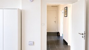 A hallway with a white wardrobe, a door with a handle, a light switch, and a thermostat on the wall. - Apartment in Barmen (Wuppertal)