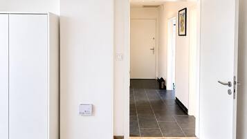 A hallway with a white wardrobe, a door with a handle, a light switch, and a thermostat on the wall.