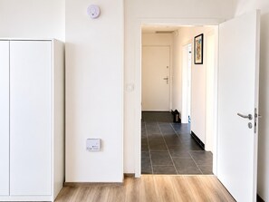 Un pasillo con un armario blanco, una puerta con pomo, un interruptor de luz y un termostato en la pared.