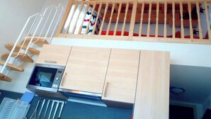 Slaapkamer in loftstijl met houten plafond, een stapelbed, een keuken met magnetron en een houten trap.