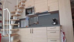 Een keuken met een magnetron, koffiezetapparaat en bestek op het aanrecht.