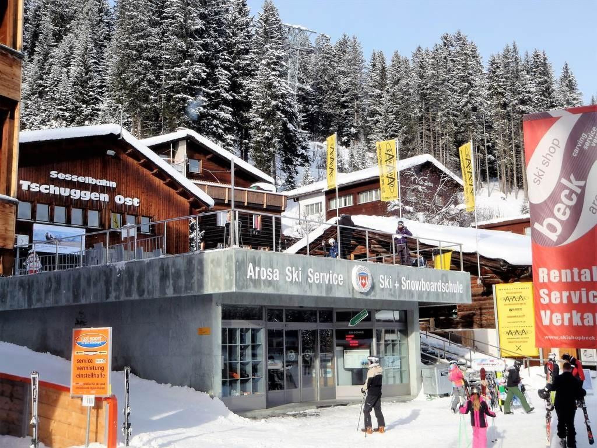 Un edificio de servicio de esquí con fachada de madera, varias ventanas y un letrero que dice Arosa Ski Service.