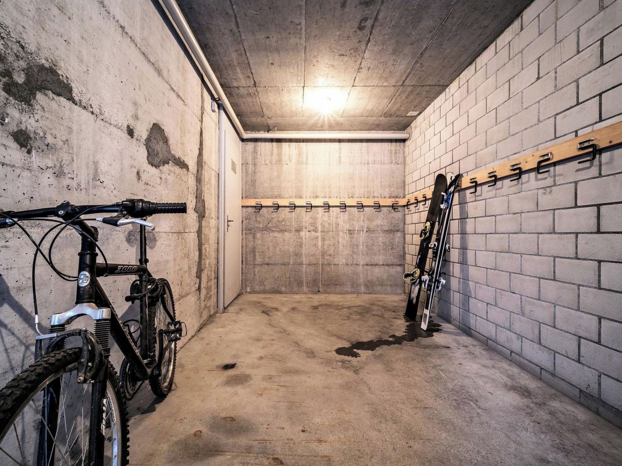 Ett rum med väggar av betong, där en cykel och ett par skidor är upphängda på hyllor.