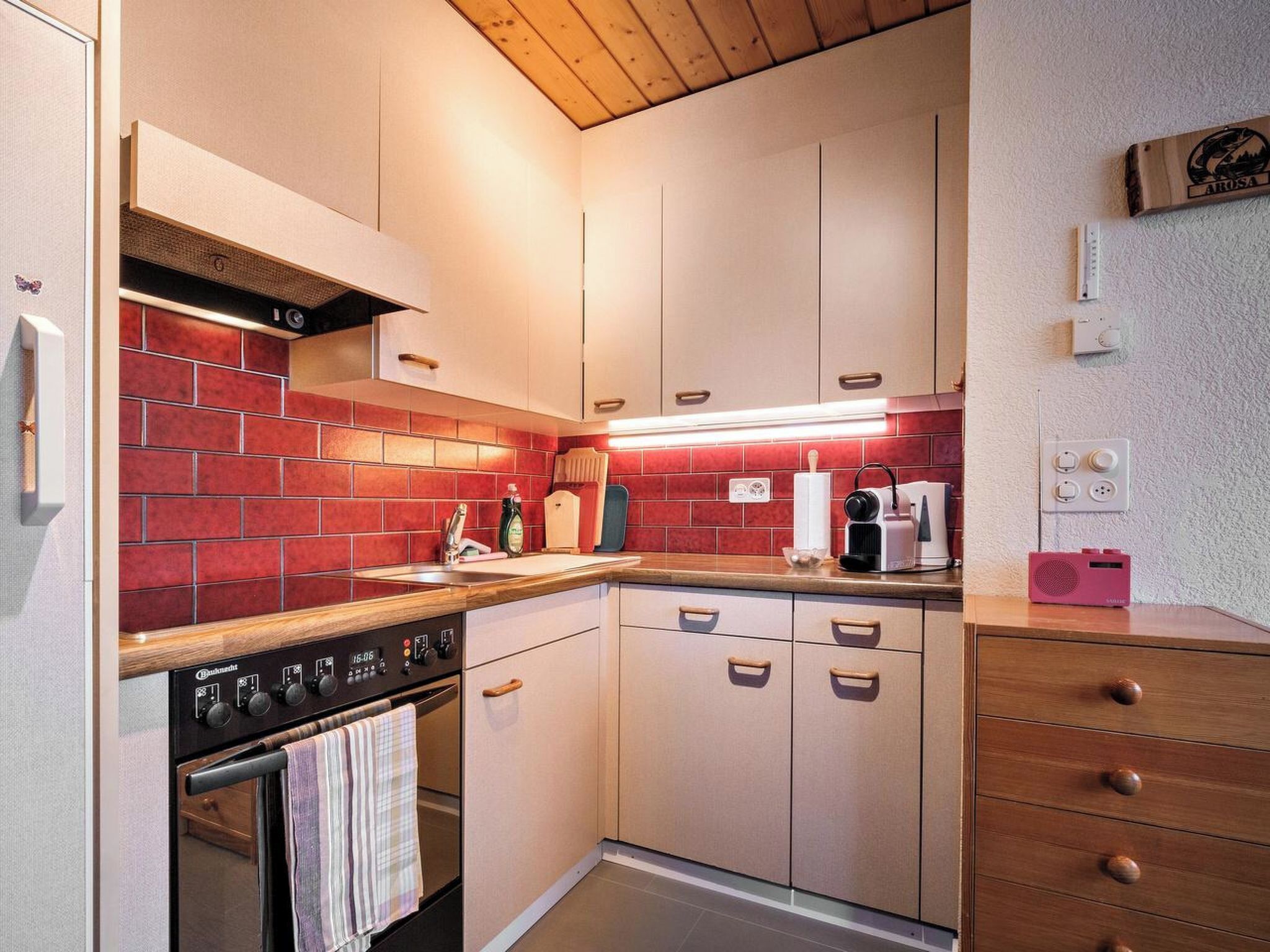 Una cucina compatta con zoccolo di piastrelle rosse, forno integrato e piano di lavoro in legno.
