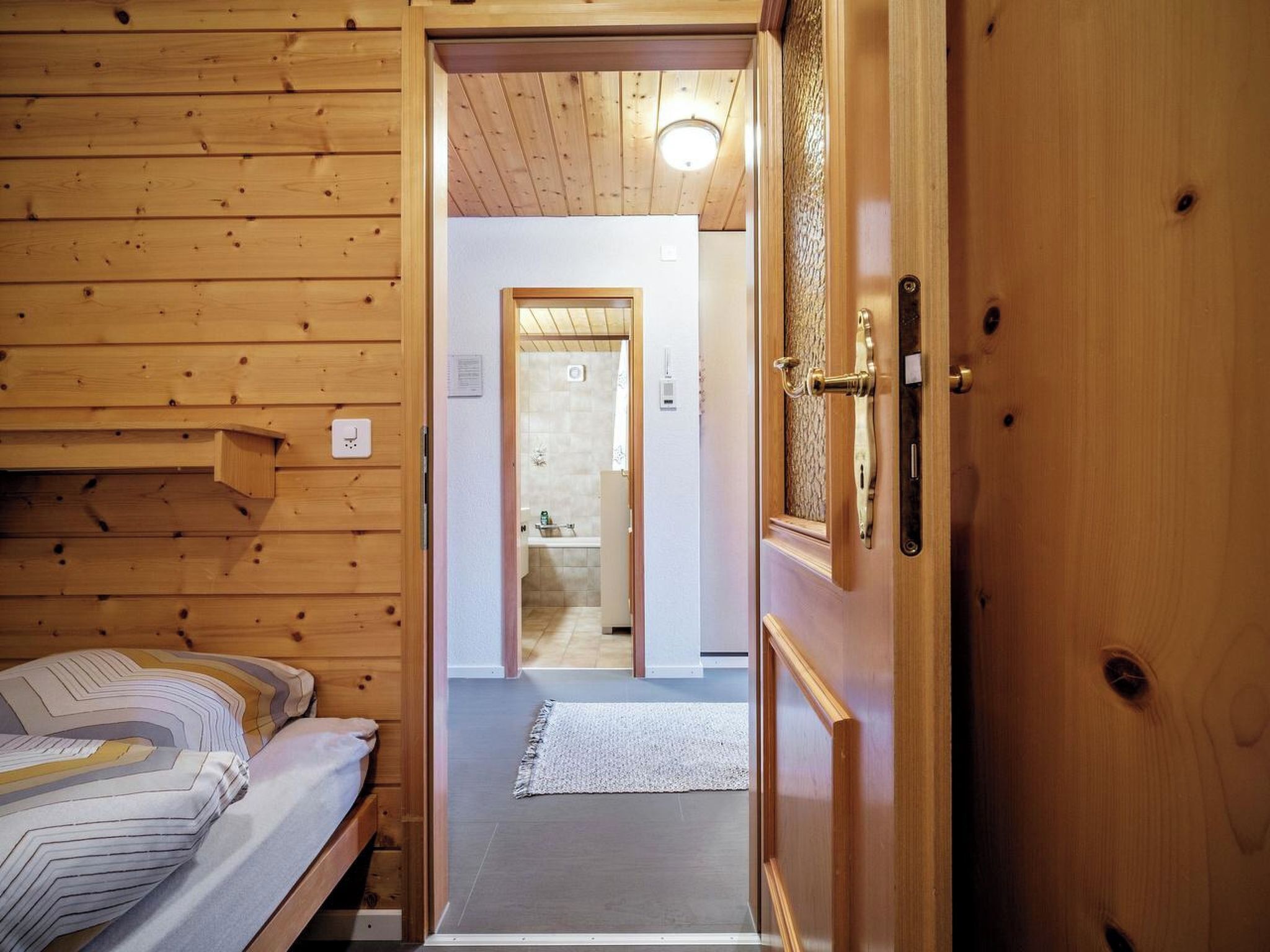 A wooden interior with a bed, a door leading to a bathroom, and a visible light fixture.
