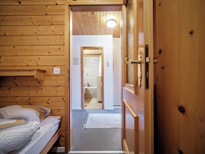 Ein Holzinterieur mit einem Bett, einer zur Toilette führenden Tür und einer sichtbaren Leuchte.