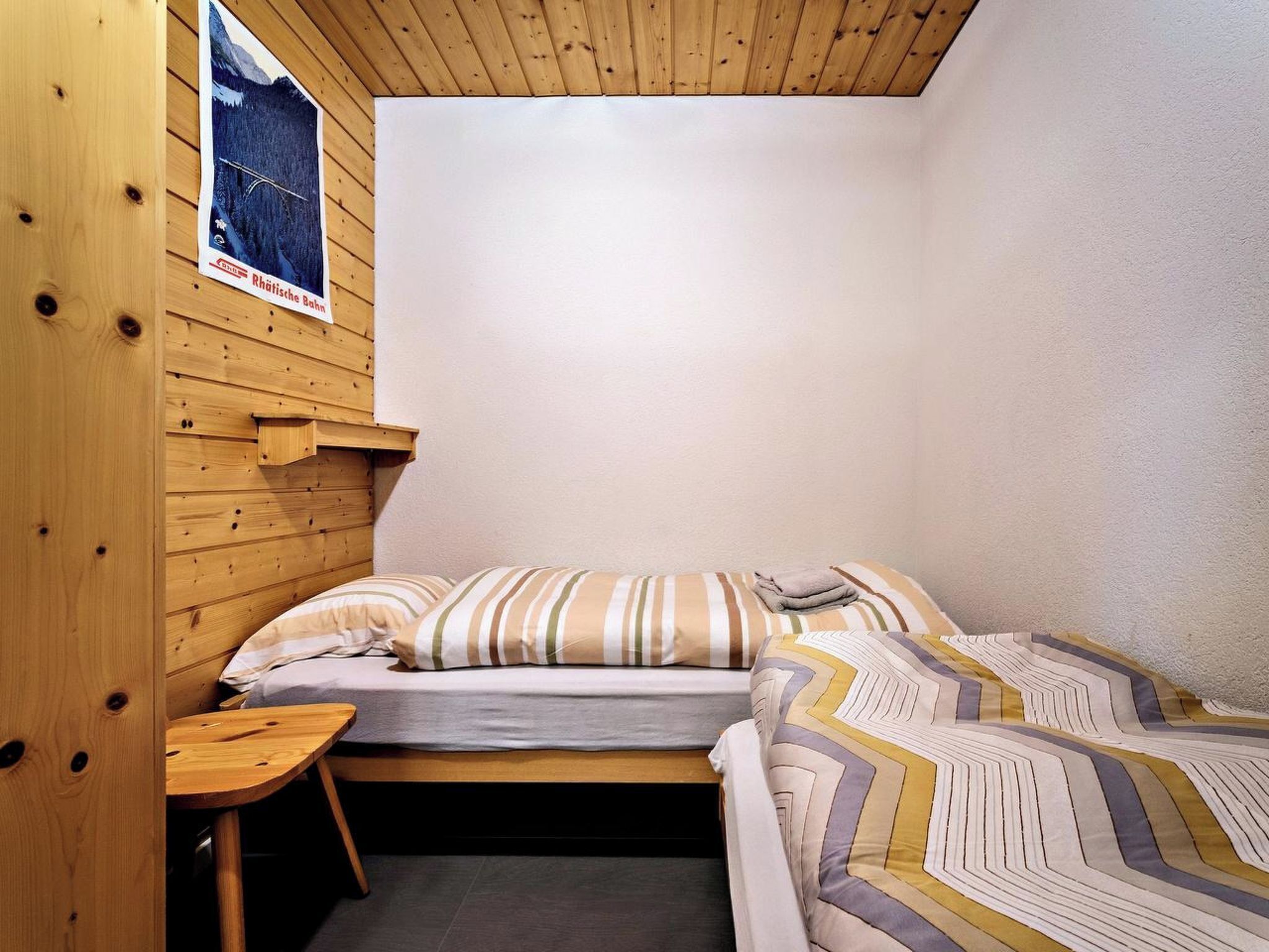 Une petite pièce en bois avec un lit superposé et un lit simple, une petite table et une affiche accrochée au mur.