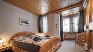 Una cama de madera con cabecera, una mesita de noche, un escritorio y un aparador en una habitación con paredes y techo de madera.