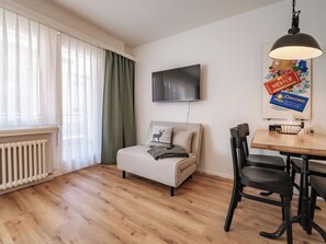 A modern living room with a sofa, a dining table with chairs, a flat-screen TV mounted on the wall, and a radiator under the window. - Paradies 212 Appartement/Fewo,  , 2-Bettwohnung 2-Bettwohnung by Interhome (Arosa)