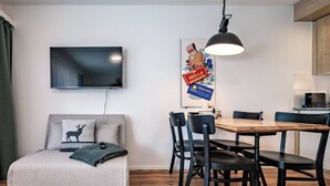 Una sala moderna con televisor de pantalla plana, un sofá con un cojín de ciervo, una mesa de comedor con sillas y una zona de cocina.