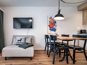 A modern living room with a flat-screen TV, a sofa with a deer pillow, a dining table with chairs, and a kitchen area. - Paradies 212 Appartement/Fewo,  , 2-Bettwohnung 2-Bettwohnung by Interhome (Arosa)