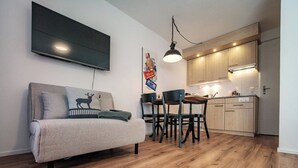 Un apartamento moderno con sofá, una mesa de comedor con sillas, una zona de cocina y un televisor de pantalla plana montado en la pared.