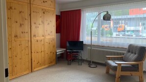 Een kamer met een houten garderobe, een televisie op een standaard, een radiator en een raam met uitzicht.