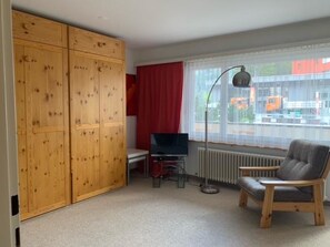 A room with a wooden wardrobe, a television on a stand, a radiator, and a window with a view of the outside. - Paradies 04 Zweibettzimmer, Dusche oder Bad, WC, 2-Bettwohnung Paradies 04 by Interhome (Arosa)