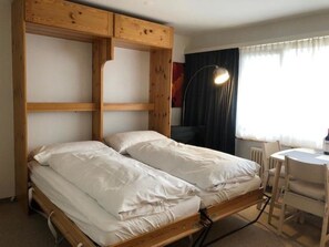 A bunk bed with a wooden frame, two white pillows, a desk with a chair, and a lamp. - Paradies 04 Zweibettzimmer, Dusche oder Bad, WC, 2-Bettwohnung Paradies 04 by Interhome (Arosa)