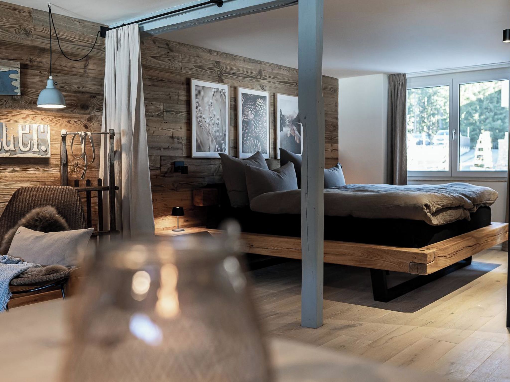 Un dormitorio moderno con cama alta, paredes de madera y un ventanal grande.