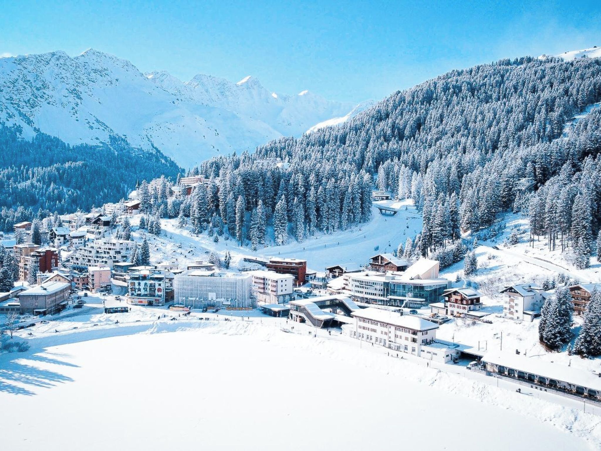 Un pueblo cubierto de nieve en la montaña, con edificios y una pista de esquí.
