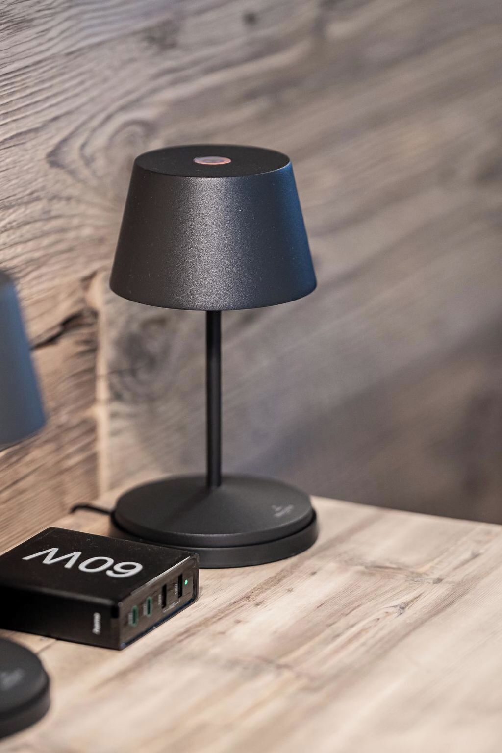 A black desk lamp with a cord and a power adapter labeled 'M09' on a wooden surface.
