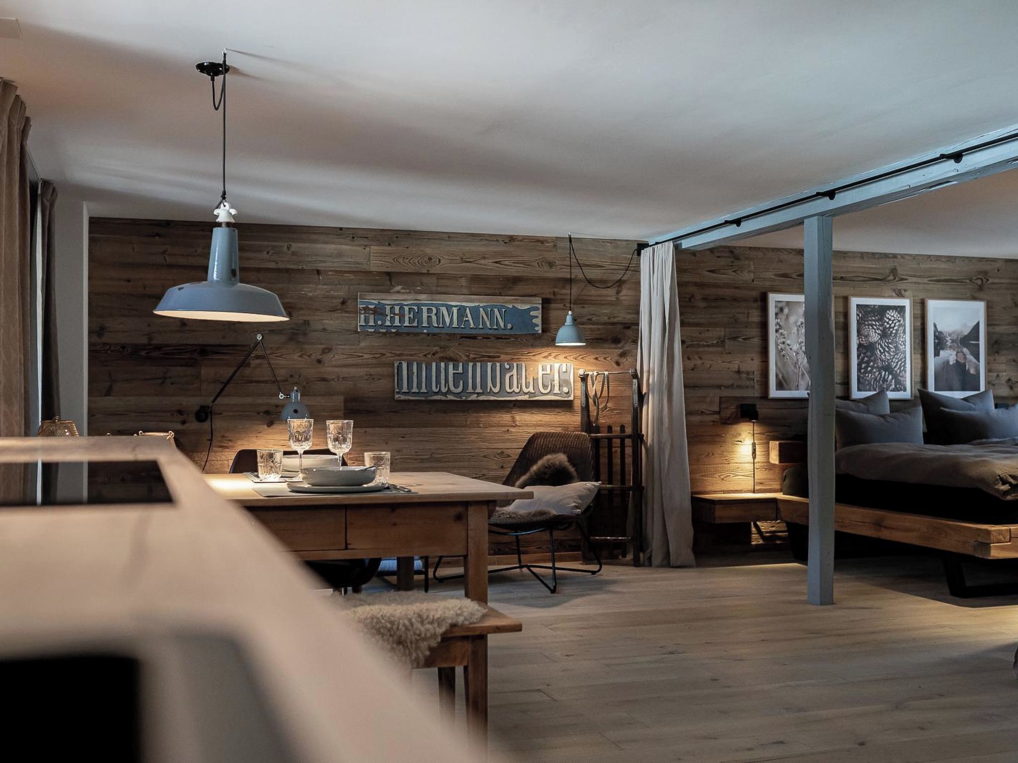 A cozy room with a wooden wall, a dining table with glasses, a chair, and a bed with pillows.