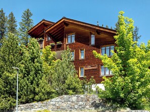 Ein mehrstöckiges Holzgebäude mit Balkonen, umgeben von Bäumen und einer Steinmauer.
