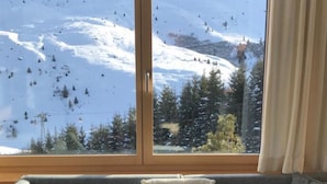 Ett rum med en soffa, ett fönster med utsikt över ett snötäckt berg och en gardin.
