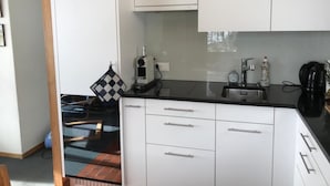 Ett kök med vita skåp, en svart bänkskiva, en kaffemaskin och en vattenkokare.