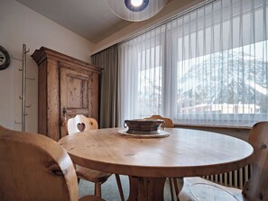 A dining room with a round wooden table, two chairs, a wooden cabinet, and a window with sheer curtains. - Paradies 045 Appartement/Fewo, Dusche, WC, 2-Bettwohnung 2-Bettwohnung by Interhome (Arosa)