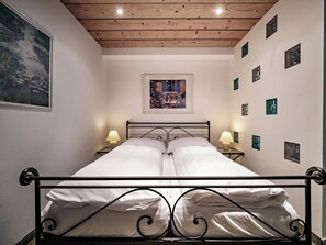 A bedroom with a bed, two bedside lamps, a framed picture above the bed, and a series of smaller pictures on the wall. - Paradies 045 Appartement/Fewo, Dusche, WC, 2-Bettwohnung 2-Bettwohnung by Interhome (Arosa)