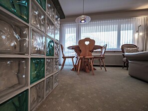 A dining area with a wooden table and chairs, a radiator, and a window with sheer curtains. - Paradies 045 Appartement/Fewo, Dusche, WC, 2-Bettwohnung 2-Bettwohnung by Interhome (Arosa)