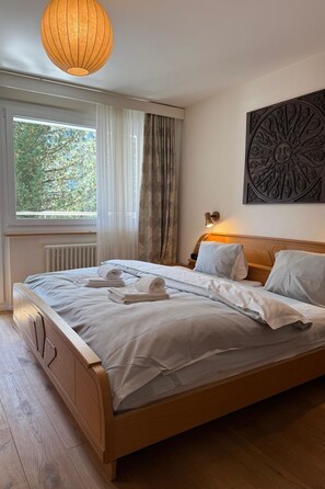 A bedroom with a wooden bed, a window with curtains, a radiator, and a wall-mounted artwork. - Casa dUval by Arosa Holiday Appartement/Fewo, Dusche, WC, 6-Bettwohnung by Interhome (Arosa)