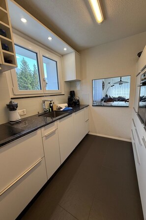 A modern kitchen with white cabinets, a black countertop, and a window overlooking a forest. - Casa dUval by Arosa Holiday Appartement/Fewo, Dusche, WC, 6-Bettwohnung by Interhome (Arosa)