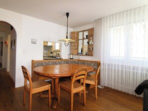 A dining area with a round wooden table and chairs, a hanging light fixture, and a window with sheer curtains. - Casa dUval by Arosa Holiday Appartement/Fewo, Dusche, WC, 6-Bettwohnung by Interhome (Arosa)