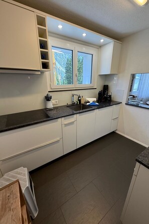 Une cuisine moderne avec des meubles blancs, un plan de travail noir et une fenêtre donnant sur des arbres.
