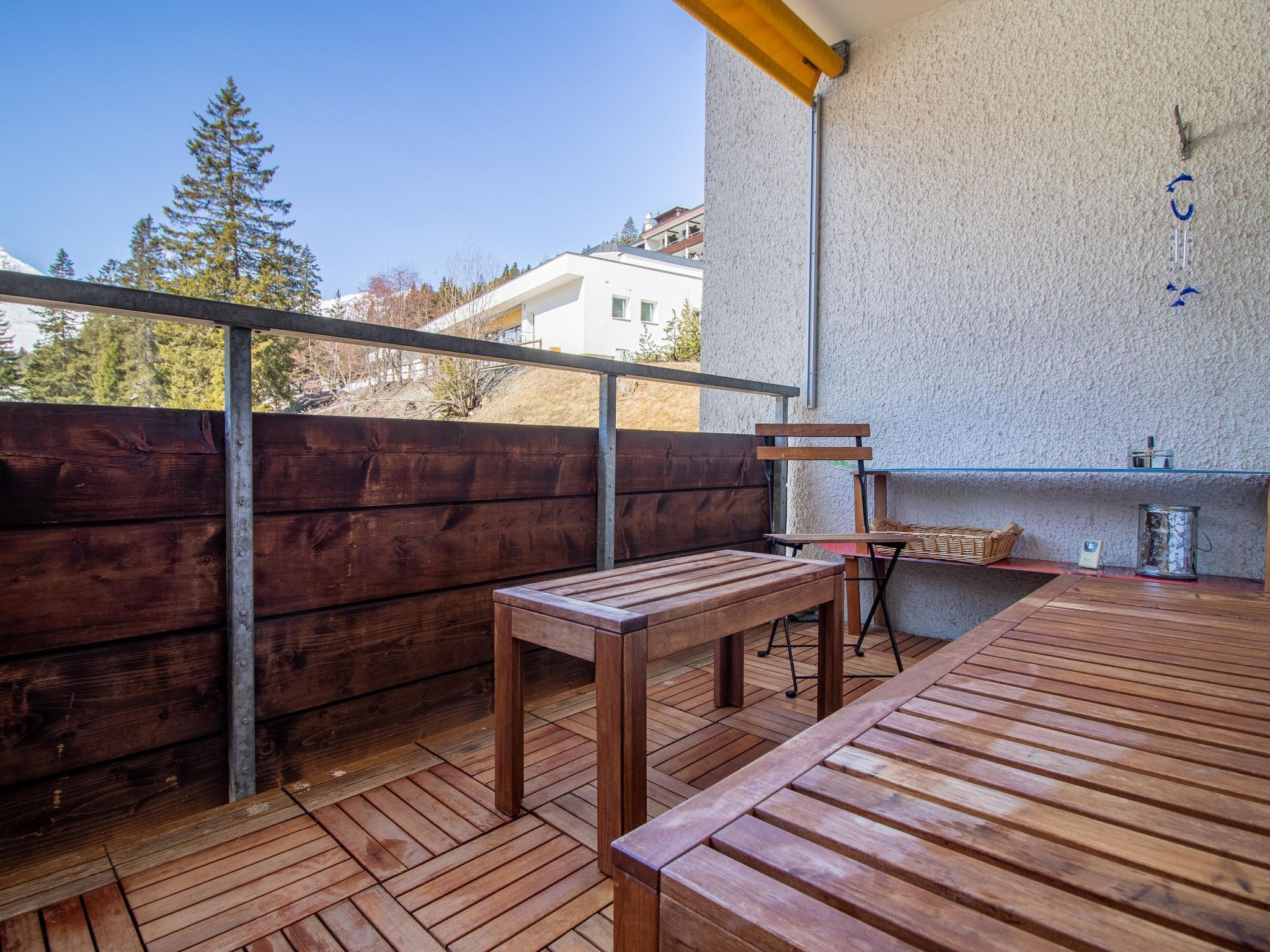 A wooden deck with a table and chairs, a barbecue grill, and a view of a white building in the background.