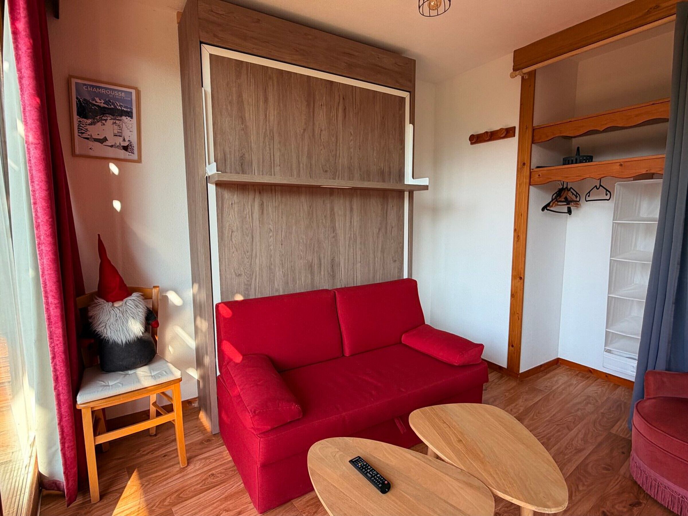 A room with a red sofa, a wooden table, a hanging coat rack, and a wall-mounted shelf.
