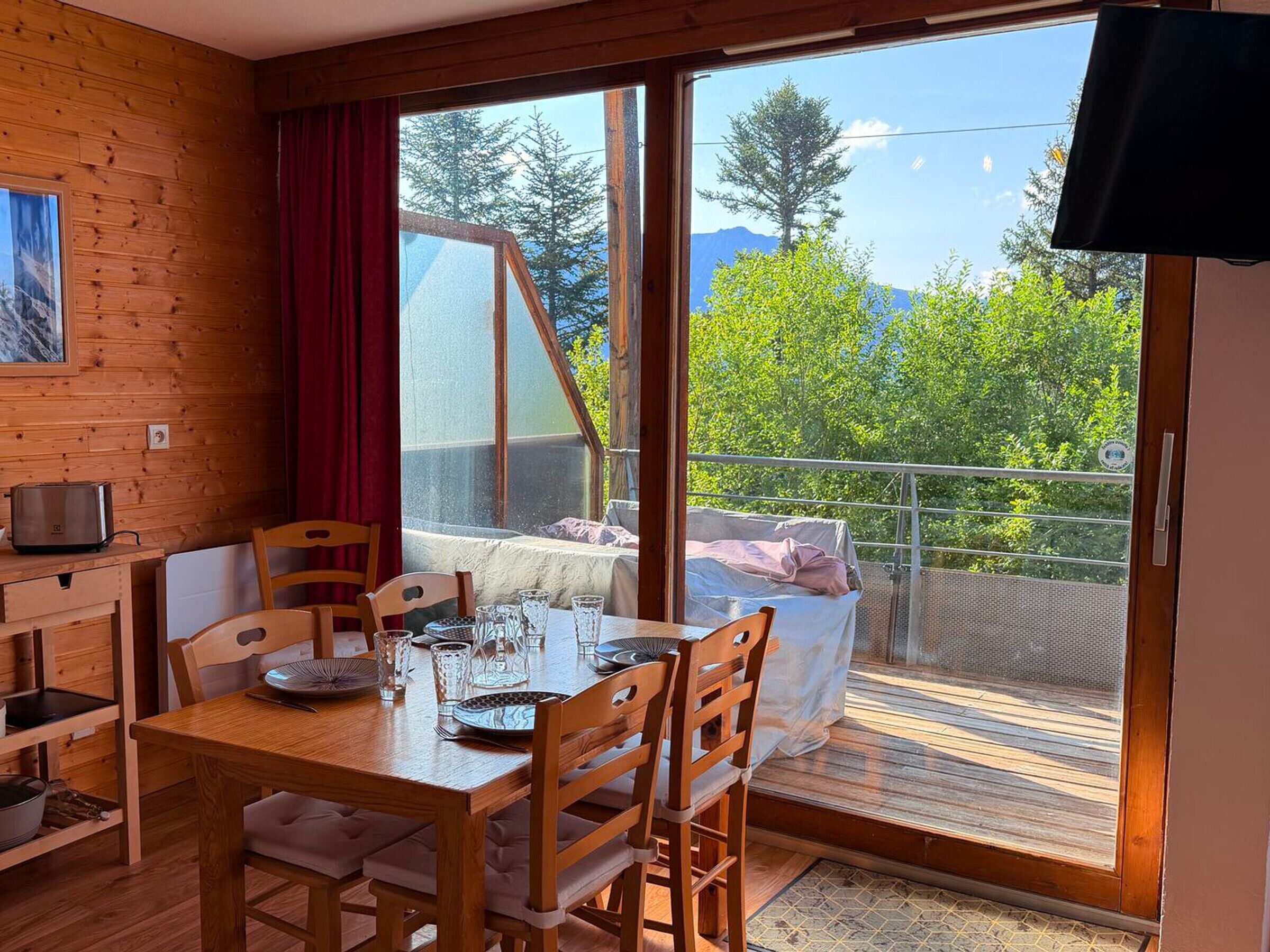 Ein Holzinterieur mit einem Esstisch für zwei Personen, einer kleinen Küchenzeile und einem Balkon mit einem Bett.