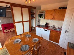 A compact kitchen with wooden cabinets, a dining table with chairs, a red sofa, and a small seating area. - Apartment in Chamrousse - 4 guests (Chamrousse)