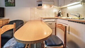 Een kleine keuken met een houten tafel en stoelen, een inbouwoven en een magnetron.