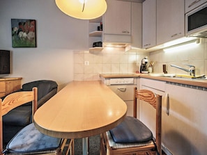 A compact kitchen with a wooden table and chairs, a built-in oven, and a microwave. - Paradies 002 Appartement/Fewo,  , 3-Bettwohnung 3-Bettwohnung by Interhome (Arosa)