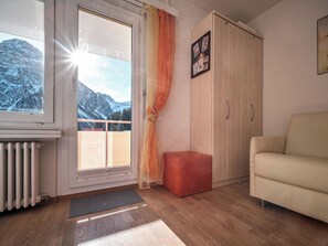 A room with a sofa, a radiator, a window with curtains, a wooden wardrobe, and a small red ottoman. - Paradies 606 Appartement/Fewo, Bad, WC, 2-Bettwohnung by Interhome (Arosa)